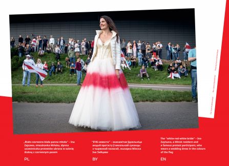 Fotografia z wystawy Białoruś. droga do wolności. młoda kobieta, ina zajcawa, ubrana w suknię ślubną z poziomym czerwonym pasem, naśladującym narodową flagę białorusi. w tle protestujący ludzie na trawiastej skarpie.